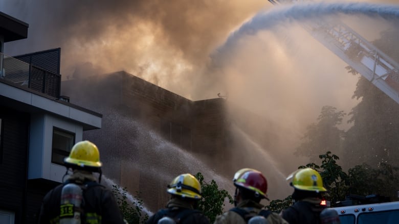 Firefighters spray water on a building shrouded in smoke.