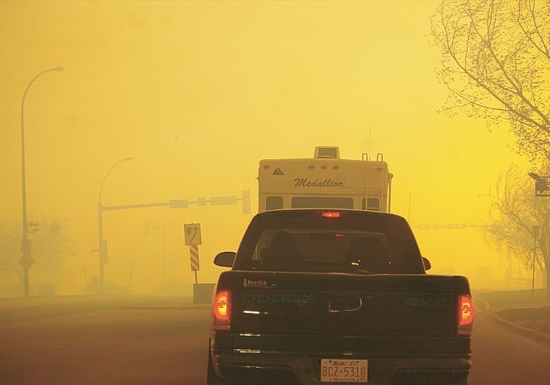 The back of a truck in a line of vehicles driving through a hazy highway.