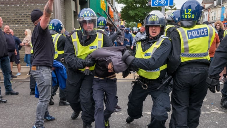 Two police officers hold on to a man they have detained.