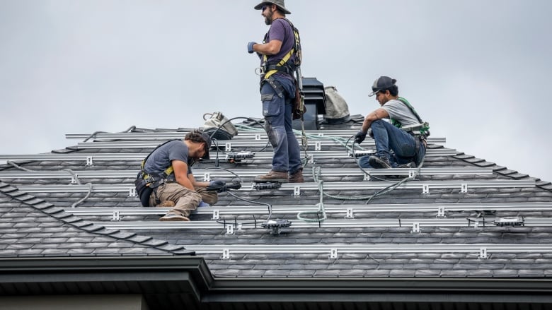 Three workers are pictured installing panels on top of a roof.