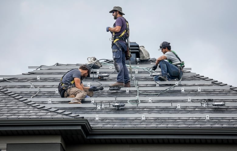 Three workers are pictured installing panels on top of a roof.