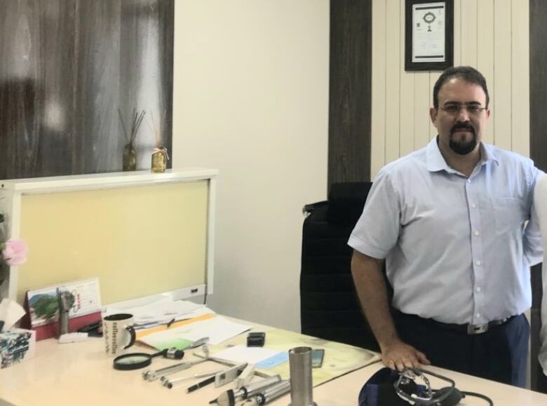 Guy with checkered shirt stands in font of desk 