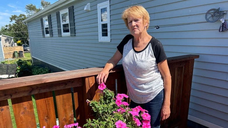 Woman standing at back of house with flowers in foreground.