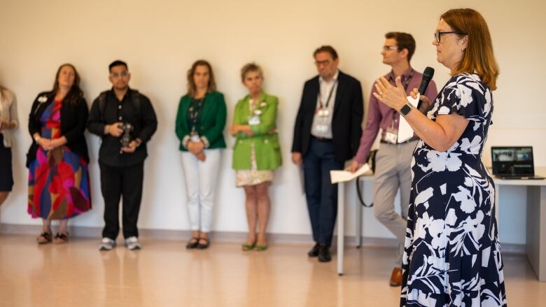 A woman holding a microphone speaks to a room.