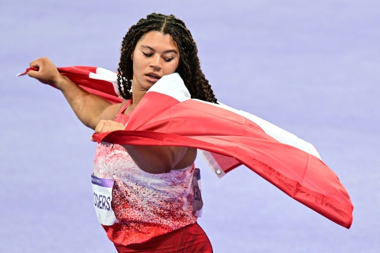 A Black woman smiles as she holds a Canadian flag behind her.