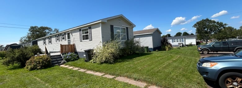 Three mini-homes placed in a row, with lawns, decks and mature shrubs surrounding them. 