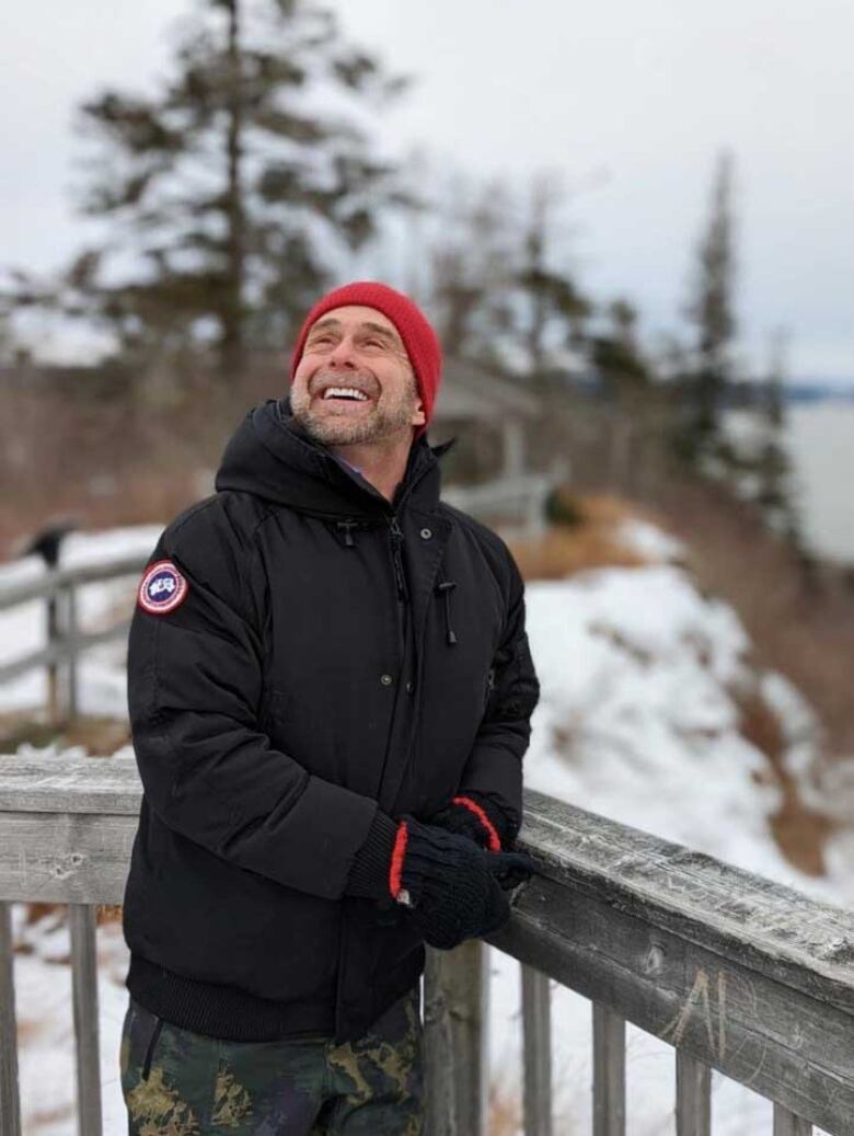 A man posing outdoors in the winter, with his head tilted back, eyes skyward, and a big smile.