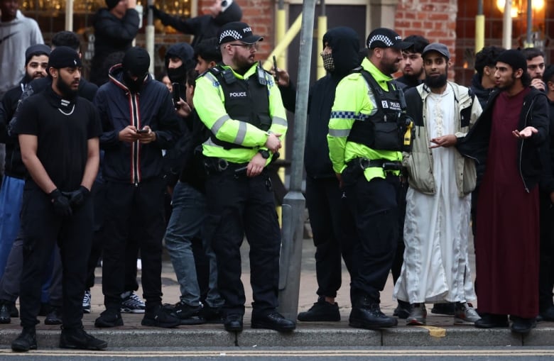 Police officers stand next to people watching an anti-racism protest.