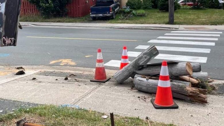 Security pylons surrounded sawed rounds of a wooden utility pole lying on a sidewalk. A crosswalk is in the rear.