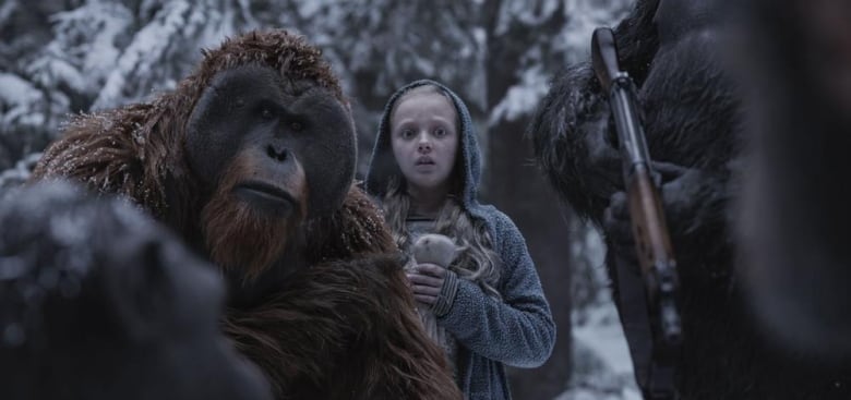 A still from the movie War for the Planet of the Apes. A CGI orangutan crouches beside a little girl in a snowy outdoor scene. 