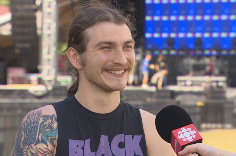 Man in Black Sabbath tank top stands in front of stage. 