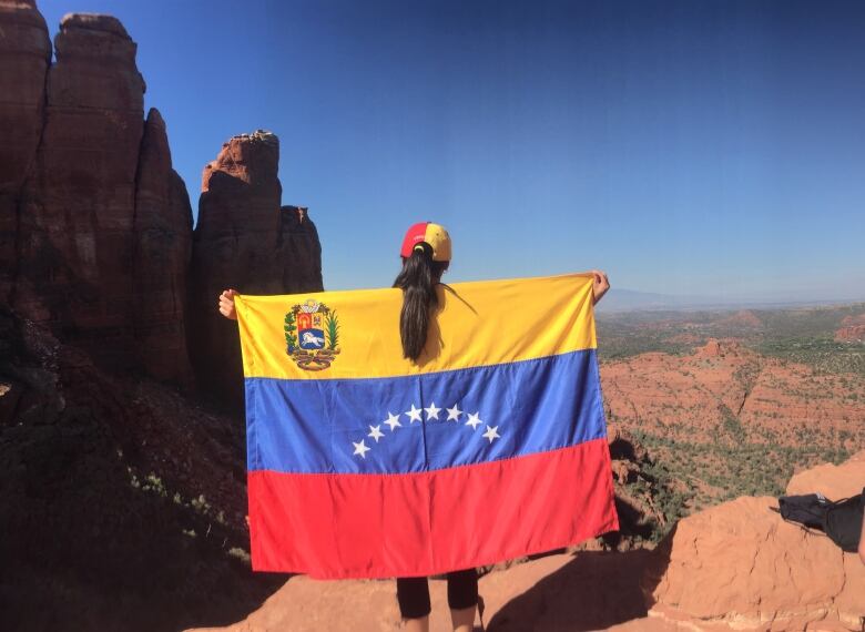 woman holds venezuelan flag on a canyon. 