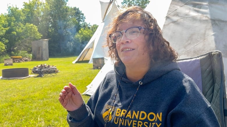 A woman sits in front of a teepee.