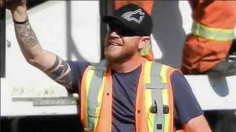 A man in an orange work vest smiles and waves. 