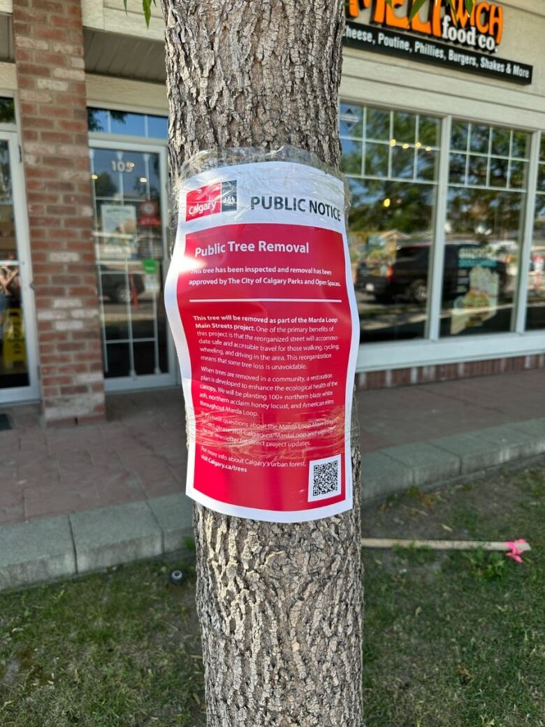 Close-up of a red sign on a tree with a restaurant in the background.