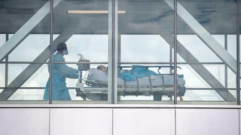 A health-care worker pushes a patient across a connecting bridge at a hospital in Montreal, Thursday, July 14, 2022, as the COVID-19 pandemic continues in the province. Over 7000 health-care workers are off the job due to COVID-19 related reasons.