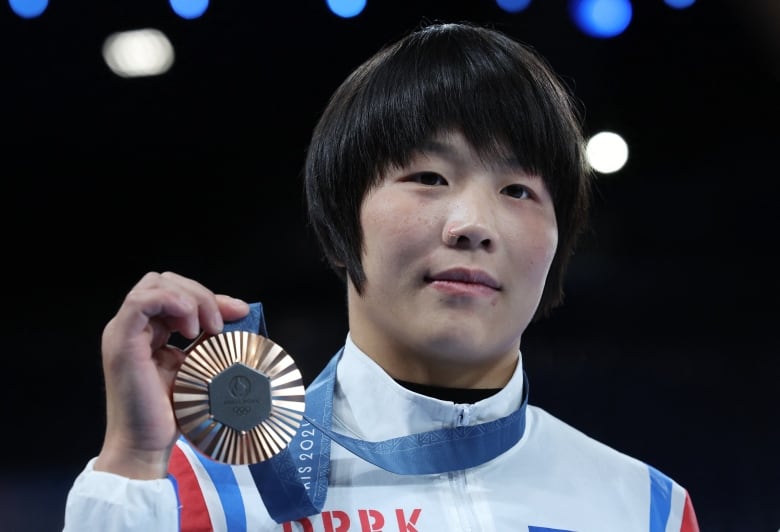 A woman holds up a bronze medal. 