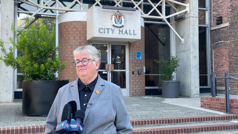 A woman with short, grey hair and a grey blazer stands in front of city hall. 