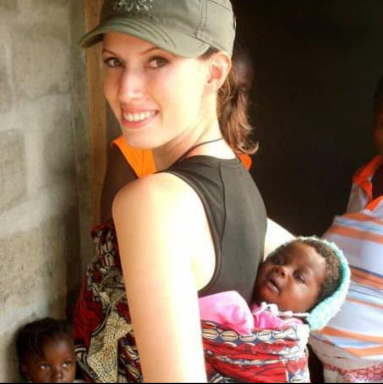 A woman holds an infant in a backpack-type carrier.