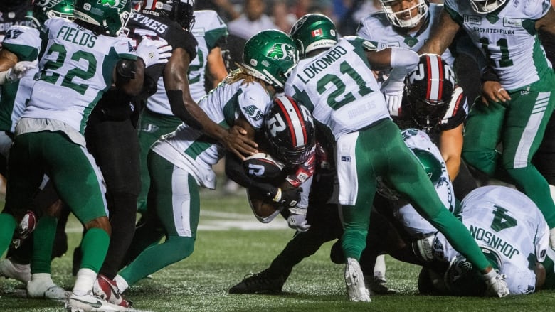 Ottawa Redblacks running back Ryquell Armstead (centre) is held up by Saskatchewan Roughriders defensive back Nelson Lokombo (21) during the first half of  CFL action in Ottawa, on Thursday, Aug. 8, 2024. 