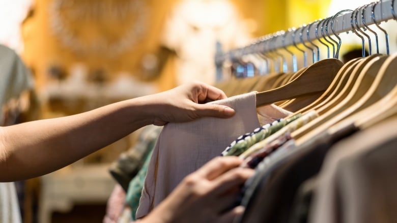 An anonymous hand lifts a sweater on a hanger off of a clothing rack