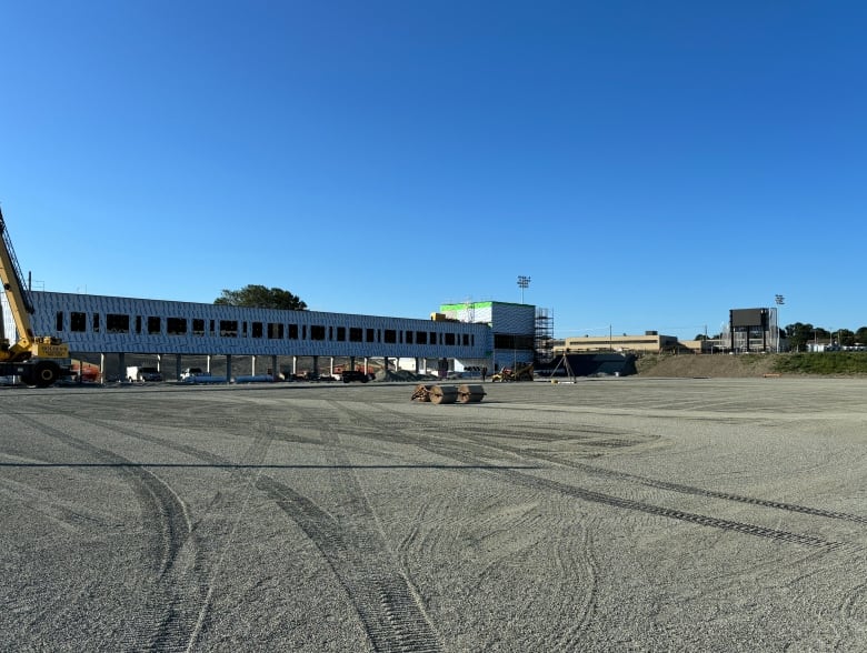 Construction tracks are visible on a flattened field of gravel. In the rear is a structure with temporary siding. 