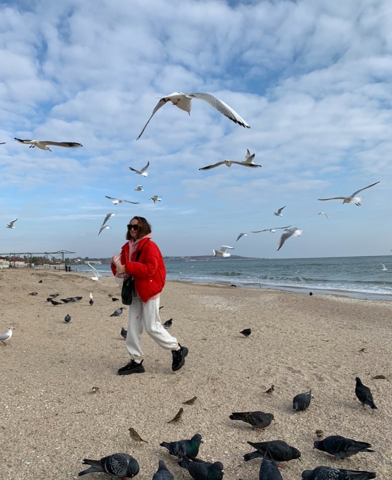 A woman walks with seagulls in front of the ocean.