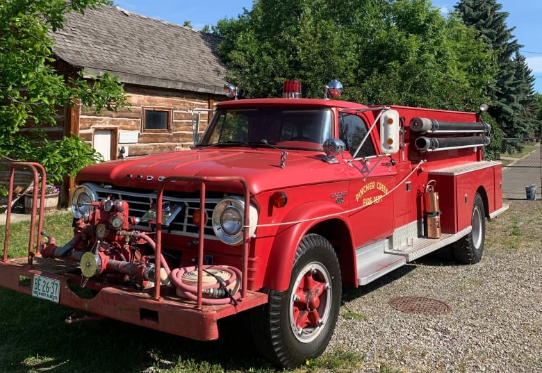 a red, vintage fire truck parked in front of a wooden house.