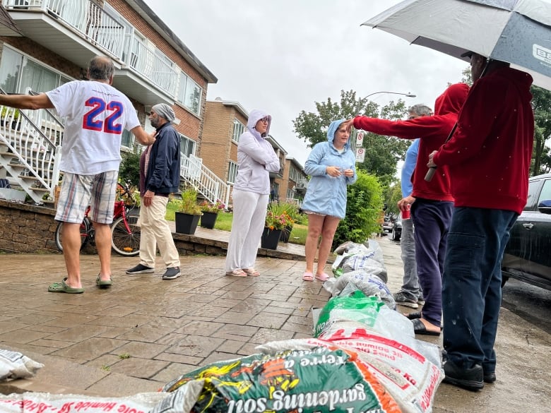 residents gather around a driveway blocked by sand bags.