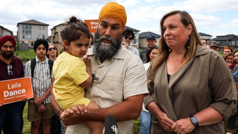 A man holding a baby stands next to a woman, in front of a group of people.