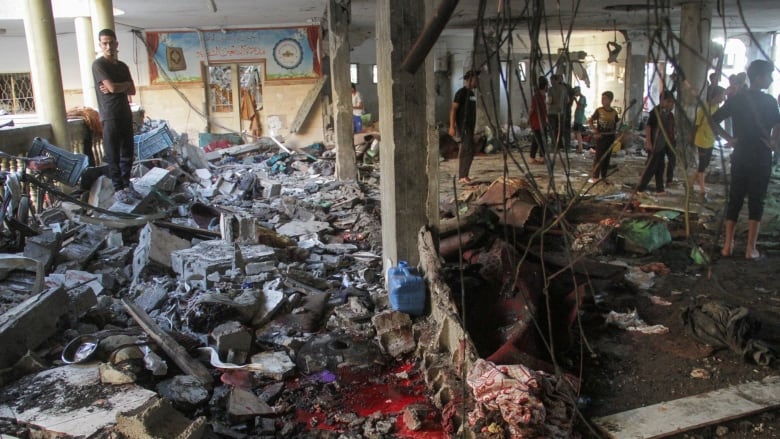 People stand amid the debris of a destroyed building.