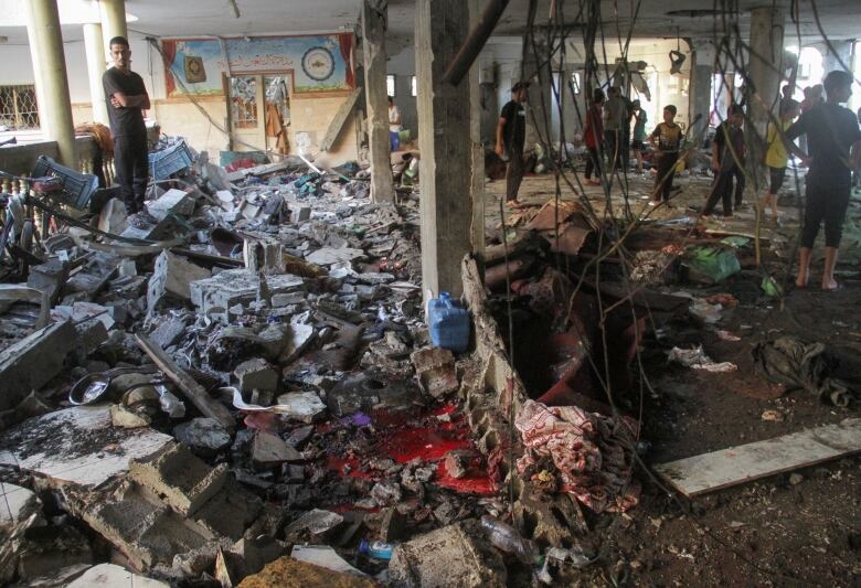 People stand amid the debris of a destroyed building.