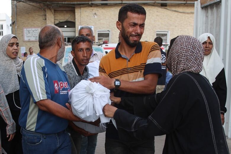 People carry a body wrapped in a white sheet.