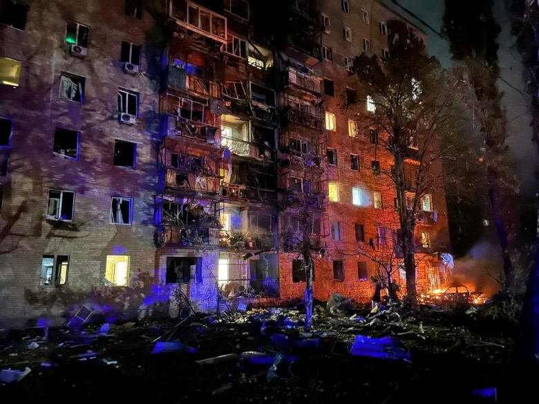 A heavily damaged apartment building at night, with fires on the ground.