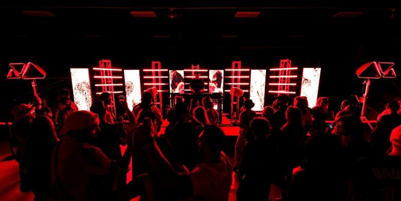 A DJ works in front of light displays in front of a crowd of people.