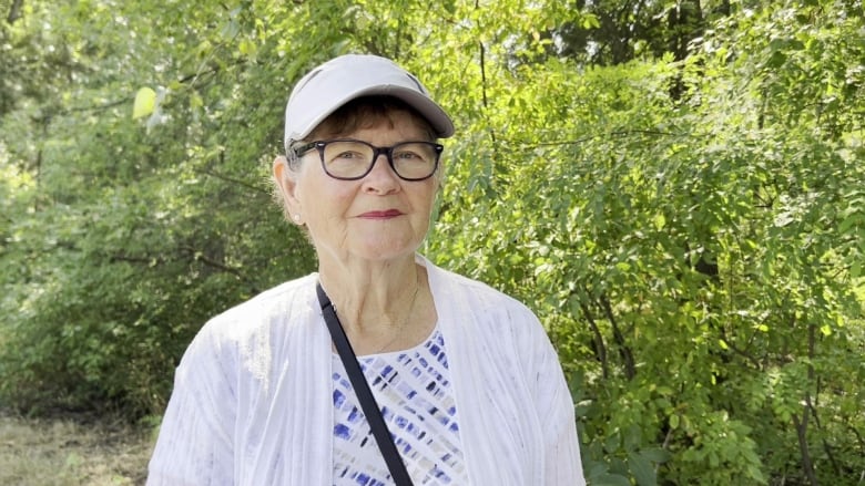 A white woman wearing a white top smiles, with greenery and plants behind her.