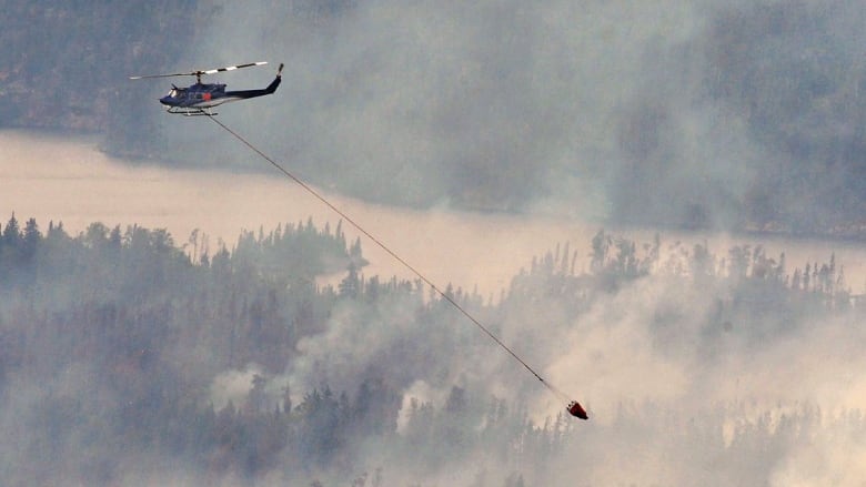 Smoke fills a wooded area and a helicopter flies overhead.