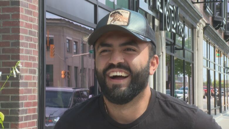 A man in a baseball cap answering questions on a sidewalk.