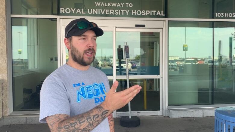 A man stands and gestures in front of the entrance to a hospital during the day.