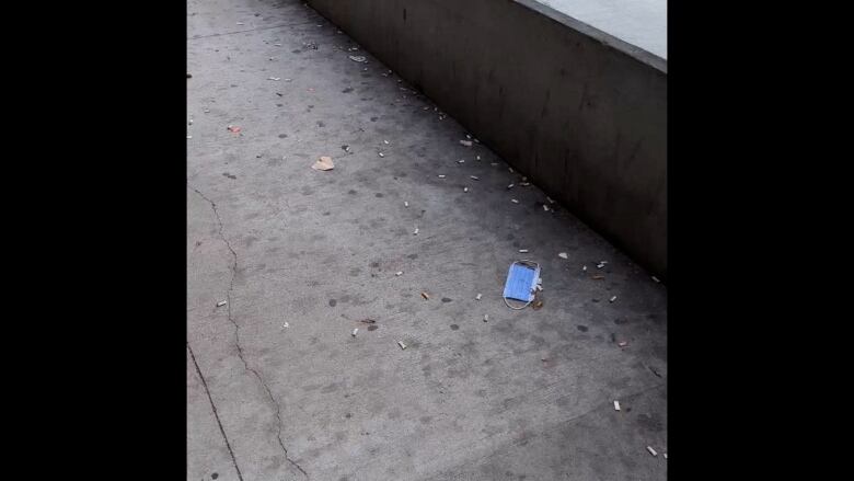 Cigarette butts and a hospital mask on sidewalk.