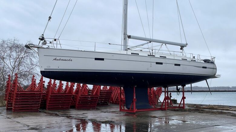 A boat is shown hoisted above the ground near a body of water.