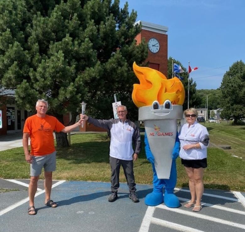 Two people standing next to a mascot shaped like a torch.