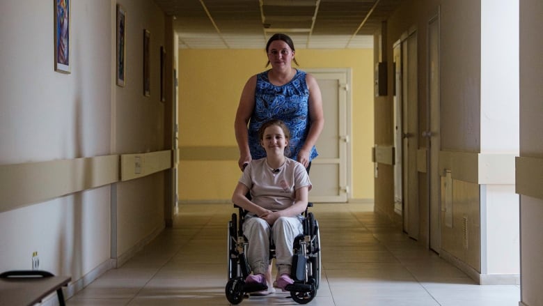 A woman wheels a young girl in a wheelchair.