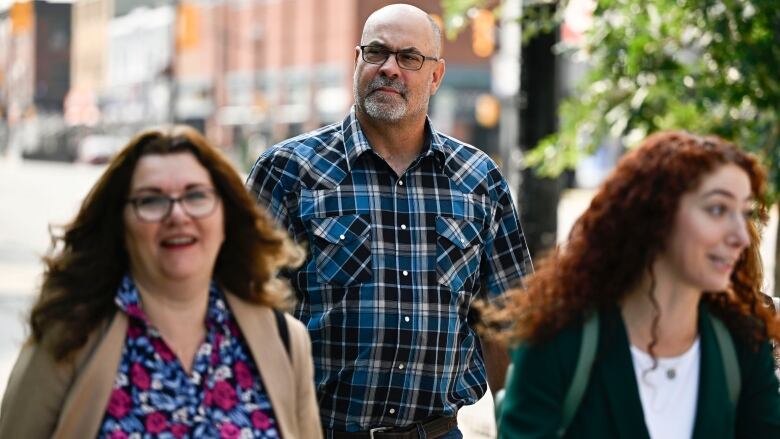 A man and two women walk down a city street.