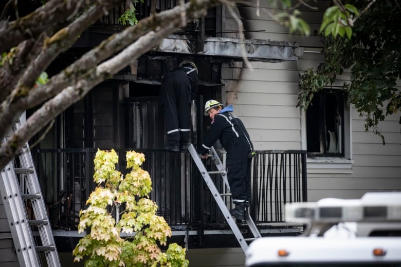 Firefighters use a ladder to reach a home that is visibly charred from a fire.