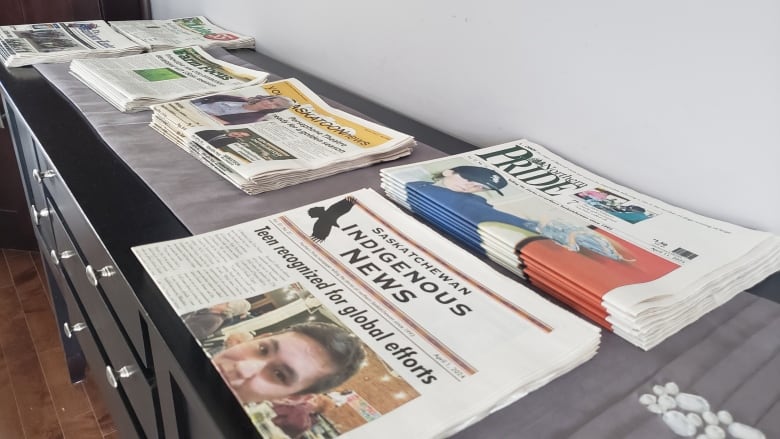 Copies of Saskatchewan Indigenous News and several other local newspapers sit in stacks on a table.