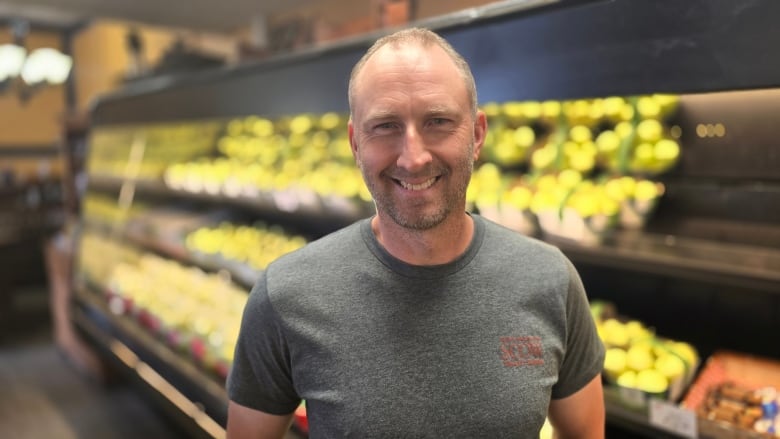 a man smiles in front of a row of green apples