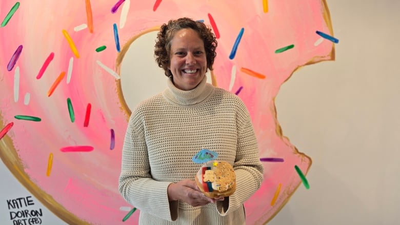 a woman holds a donut in front of a pink mural