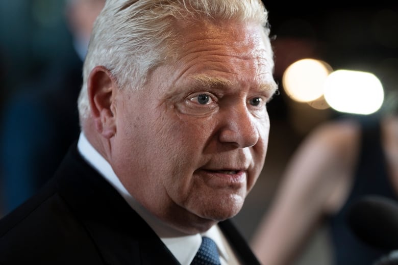 An extreme closeup of Doug Ford at a press conference. He is wearing a dark suit and tie