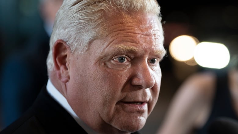 An extreme closeup of Doug Ford at a press conference. He is wearing a dark suit and tie